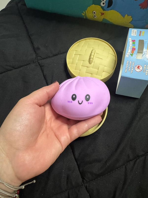 Hand holding pink mystery dumpling squishy beside opened bamboo steamer box - unboxing moment